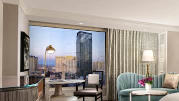 A hotel room with a large window offering a city view, a round table, a sofa, and a lamp.