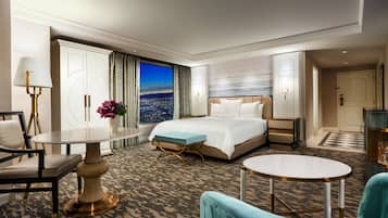 A hotel room with a large bed, a desk, a chair, a small table, and a view of the city at night.