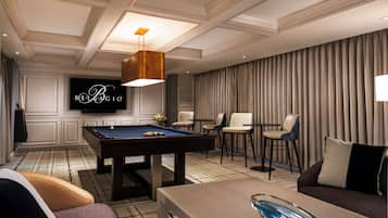 A billiards table, a pool cue, a sofa, a TV, and a chandelier in a hotel room.