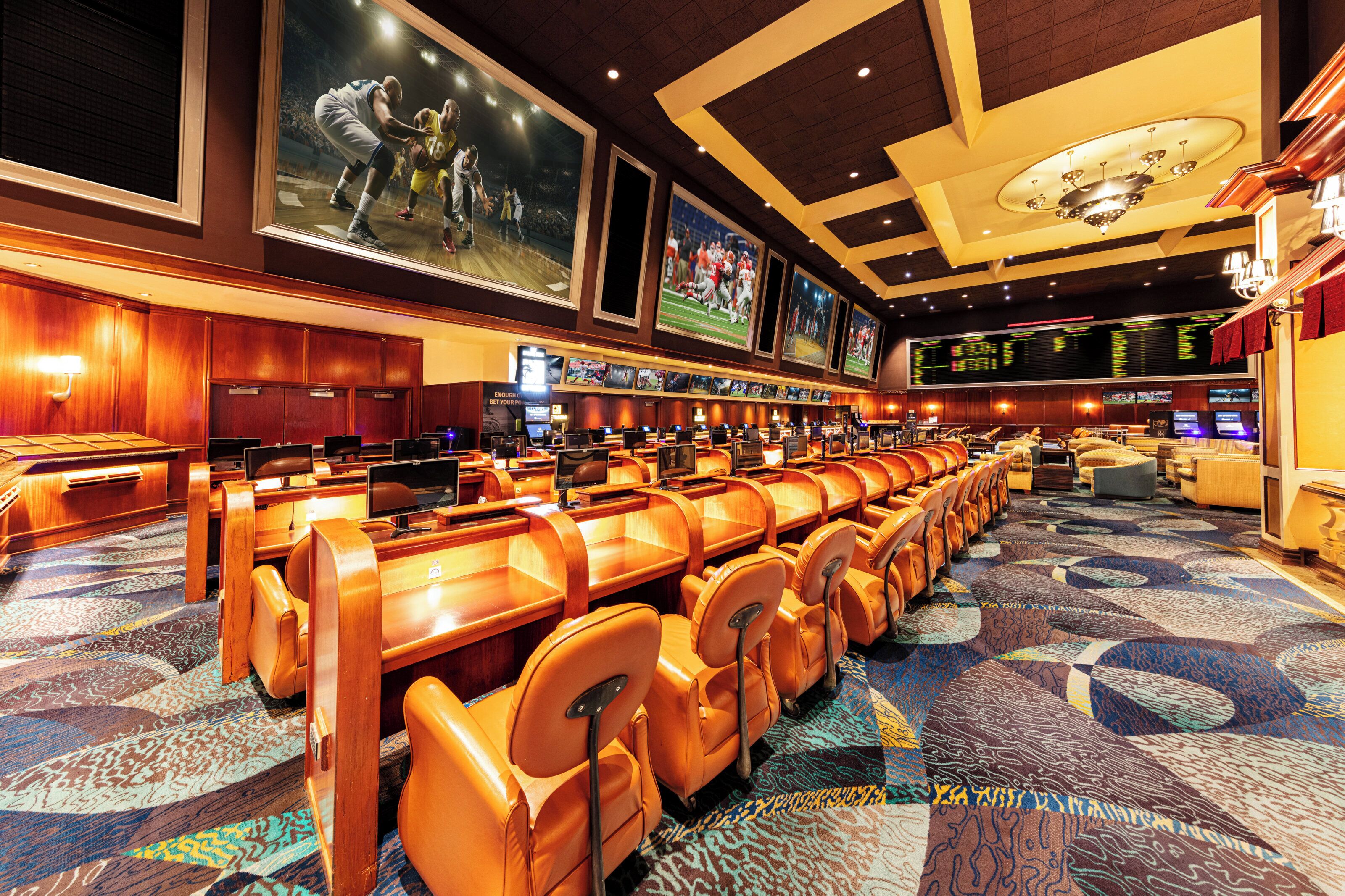 A hotel lobby with rows of leather chairs, a large screen displaying sports, and a carpeted floor.