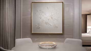 A modern hotel room with a dining area featuring a white table, a clear glass bowl centerpiece, and a framed floral artwork on the wall.