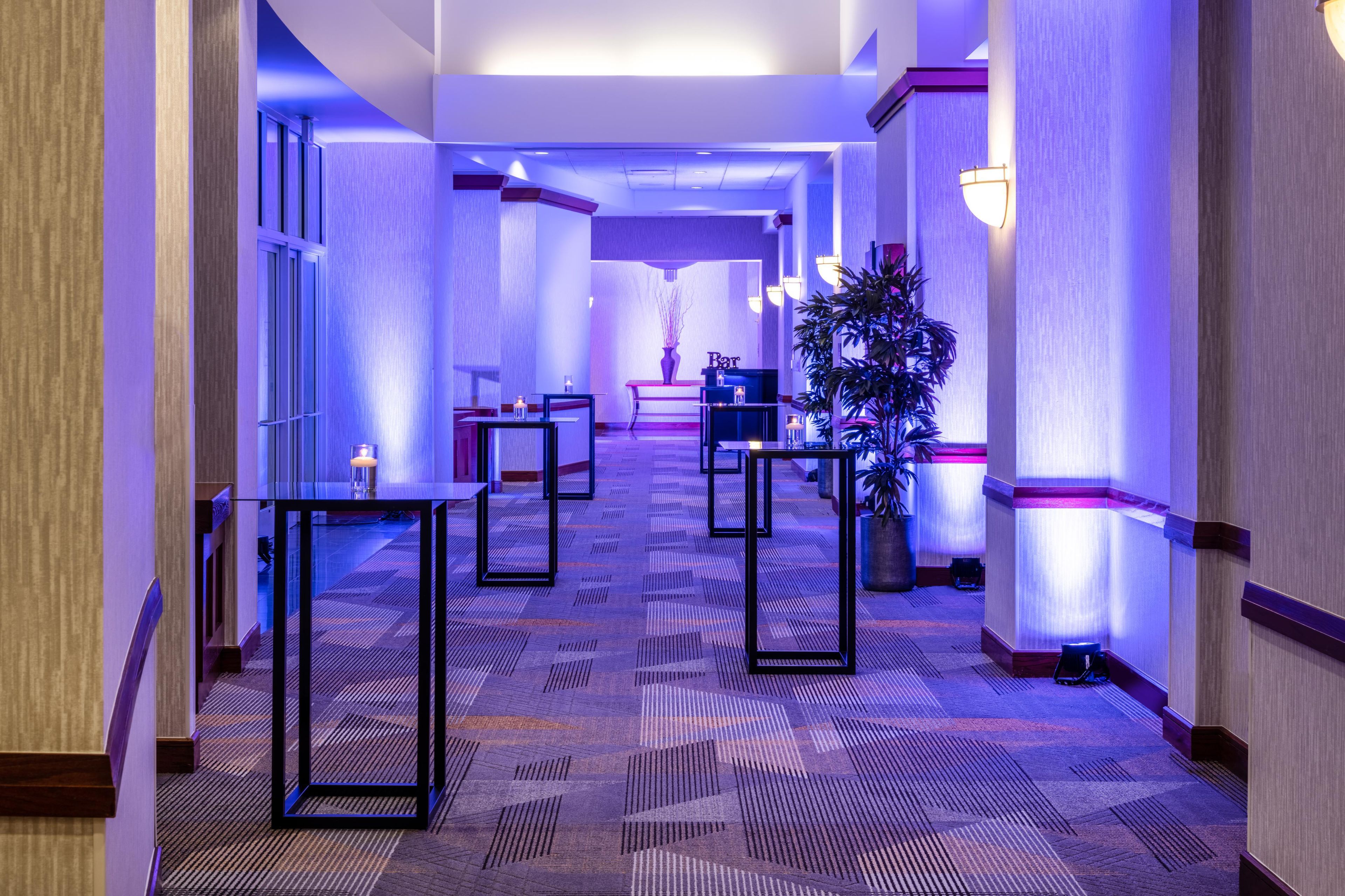 Un pasillo de hotel con alfombra estampada, muebles modernos e iluminación ambiental.