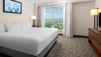 A hotel room with a bed, a TV, a window with curtains, and a painting on the wall.