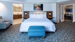 A hotel room with a large bed, a sitting area with a chair, a desk, and a view of the bathroom. - Embassy Suites by Hilton Portland Airport (Portland)