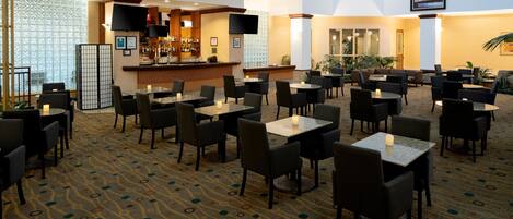 A hotel lobby with a bar area, multiple seating arrangements, and a patterned carpet.