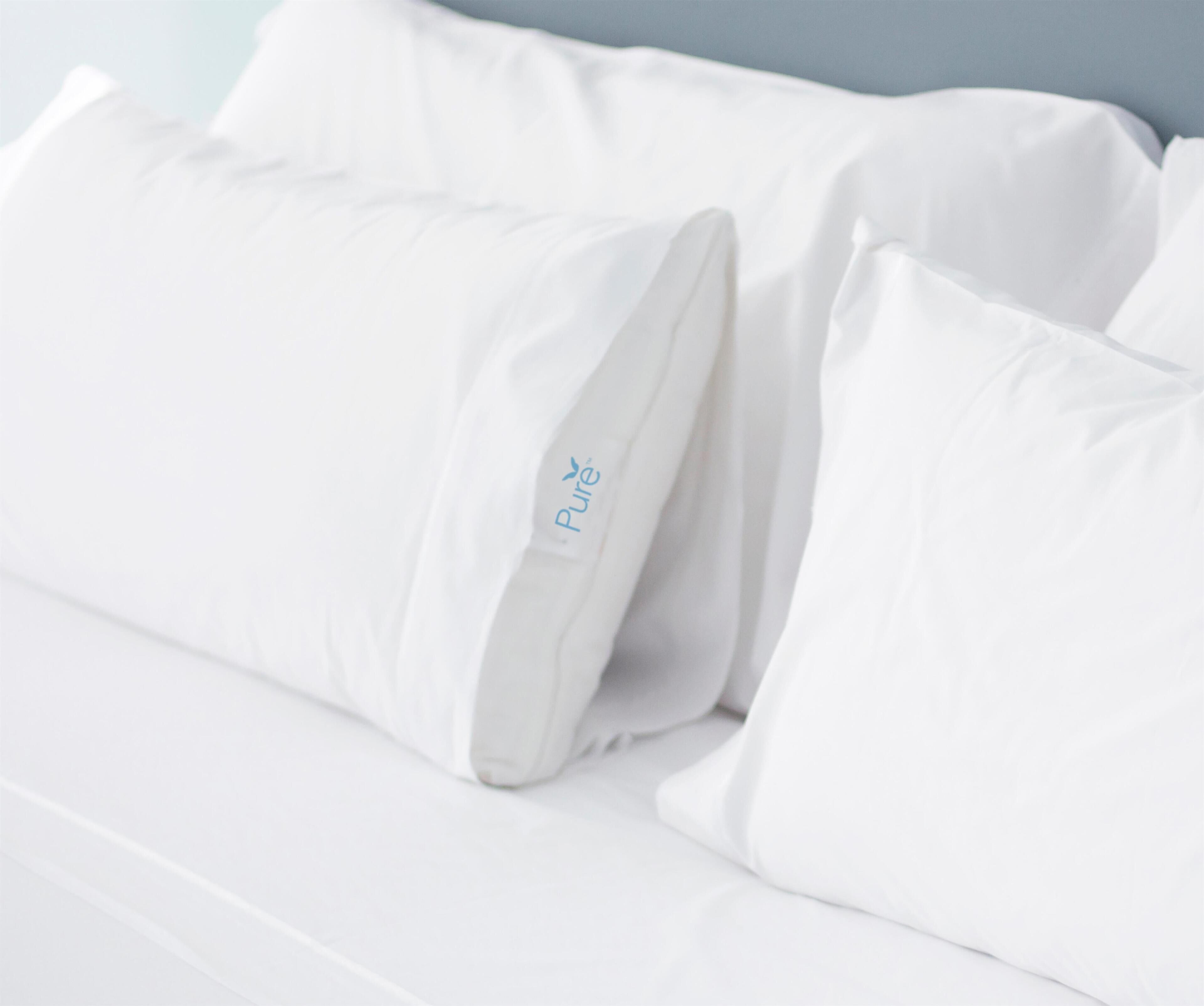 A bed with white bedding and pillows, one of which has a visible brand logo.