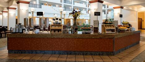Vestíbulo de hotel con mostrador de recepción central, varios pisos visibles al fondo y diversas comodidades, como una exhibición de frutas y áreas de descanso.