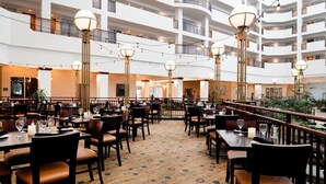 A multi-level hotel lobby with dining tables, chairs, and a patterned carpet. - Embassy Suites by Hilton Portland Airport (Portland)