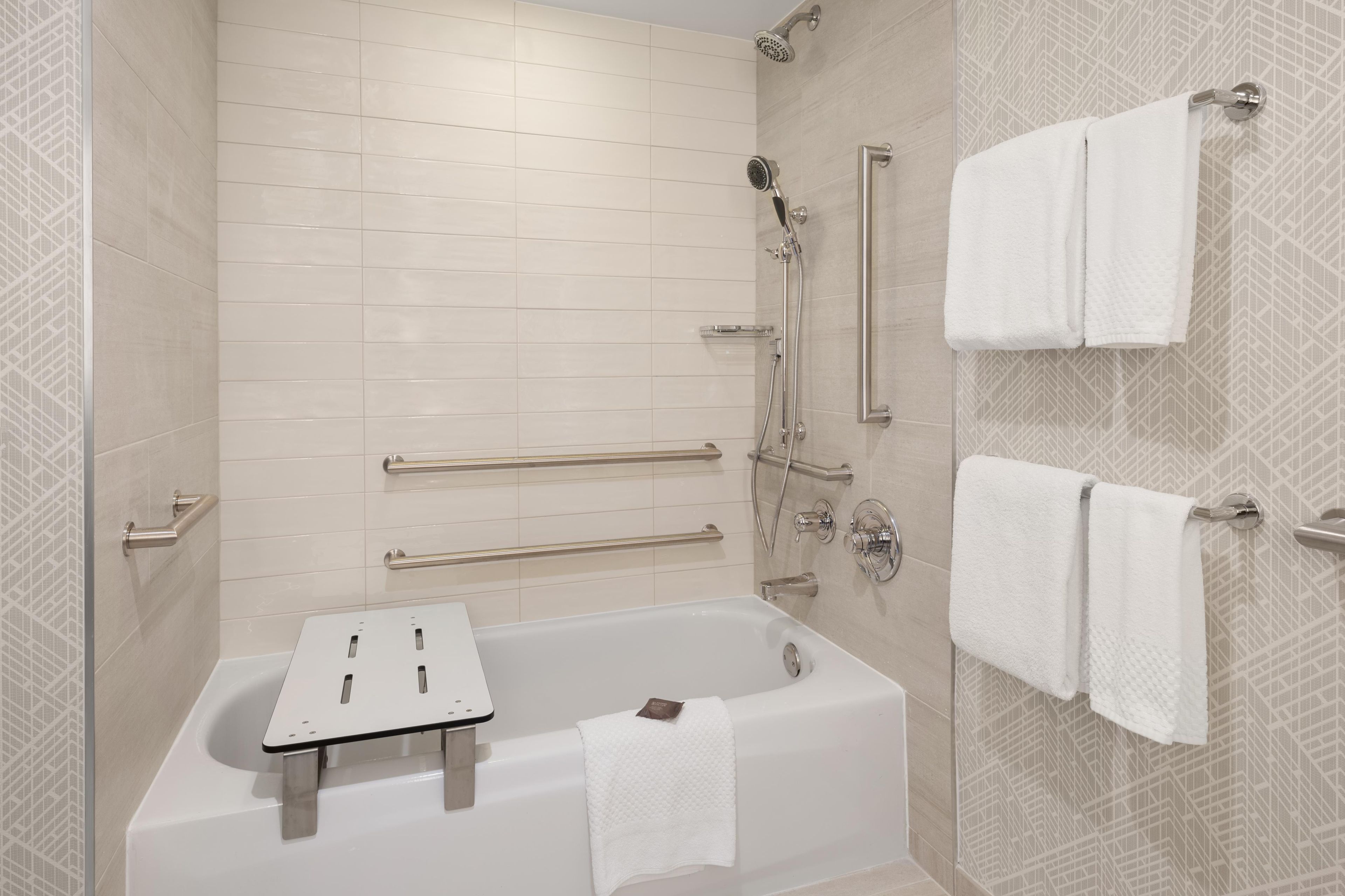 A modern bathroom with a bathtub, shower, and handrails.