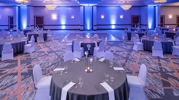 Un salón de banquetes con mesas redondas, sillas blancas y candelabros.