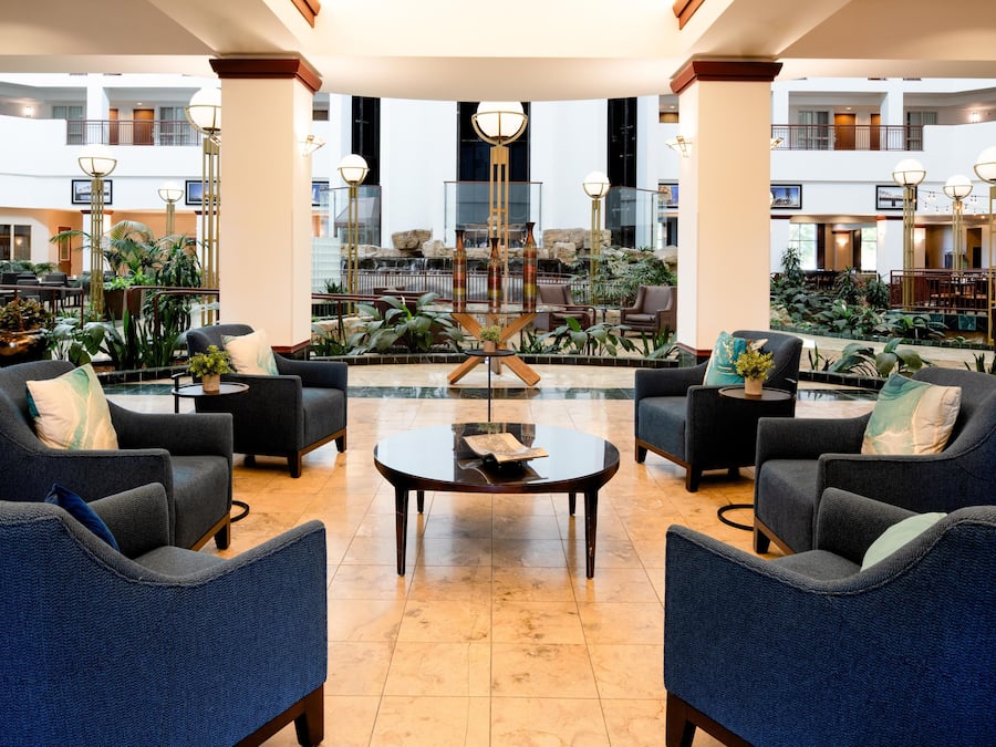 A spacious lobby with a central coffee table, seating area with sofas, and a view of a waterfall and indoor garden.