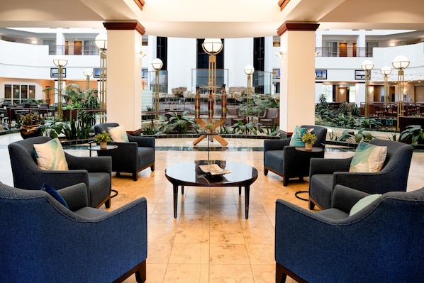 A spacious lobby with a central coffee table, seating area with sofas, and a view of a waterfall and indoor garden.