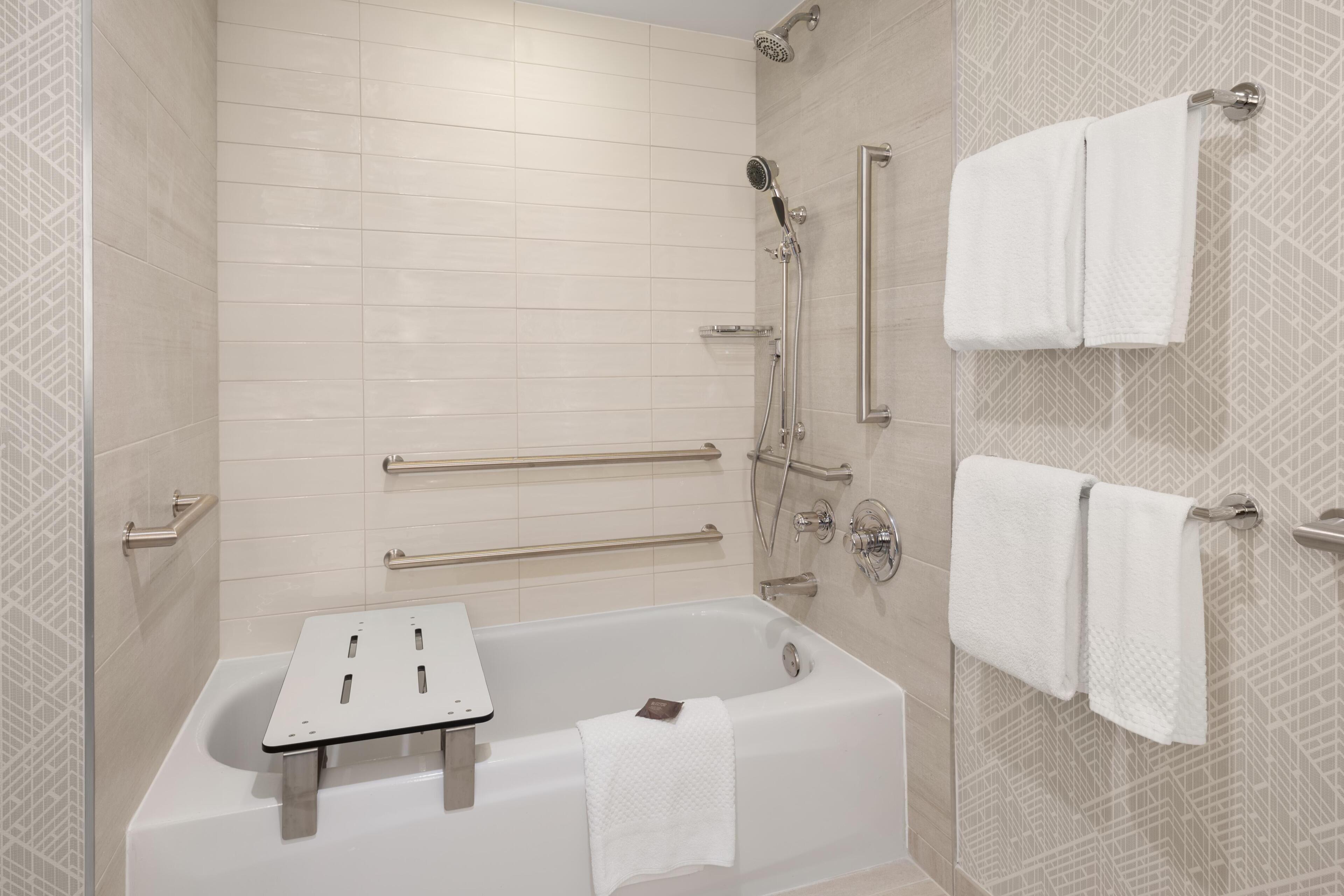A modern bathroom with a bathtub, shower, handrails, and a towel rack.