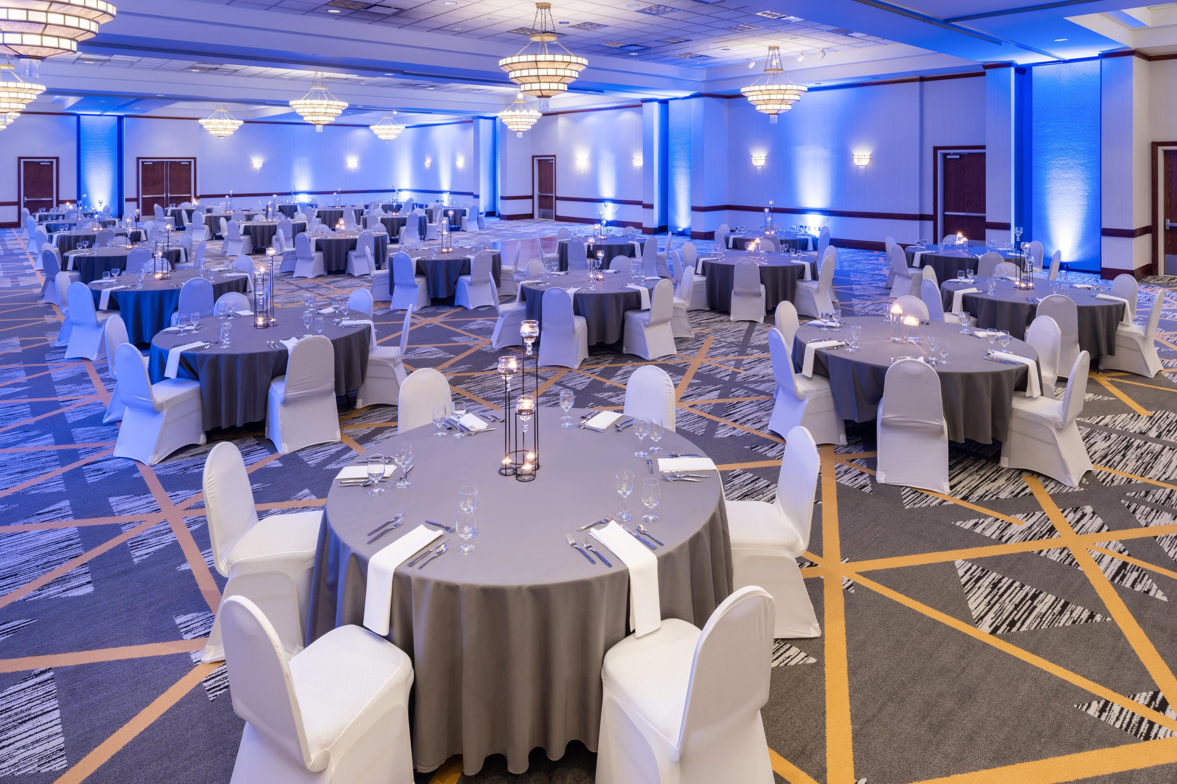 Um amplo salão de banquetes com mesas redondas, cadeiras brancas e carpete azul.
