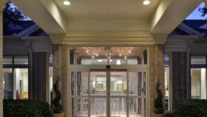 L’entrée d’un hôtel, avec une porte en verre, des colonnes en briques et une allée couverte.