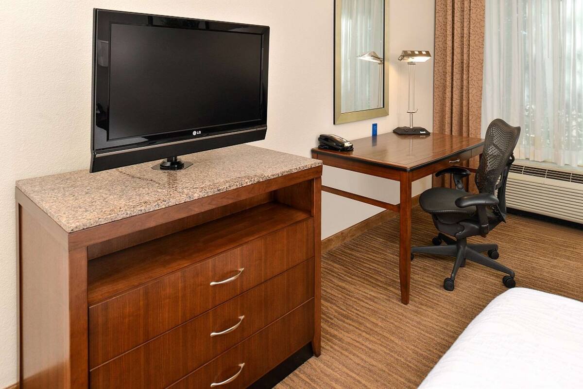 Habitación de hotel con televisión de pantalla plana, escritorio de madera, silla, cómoda y cama.