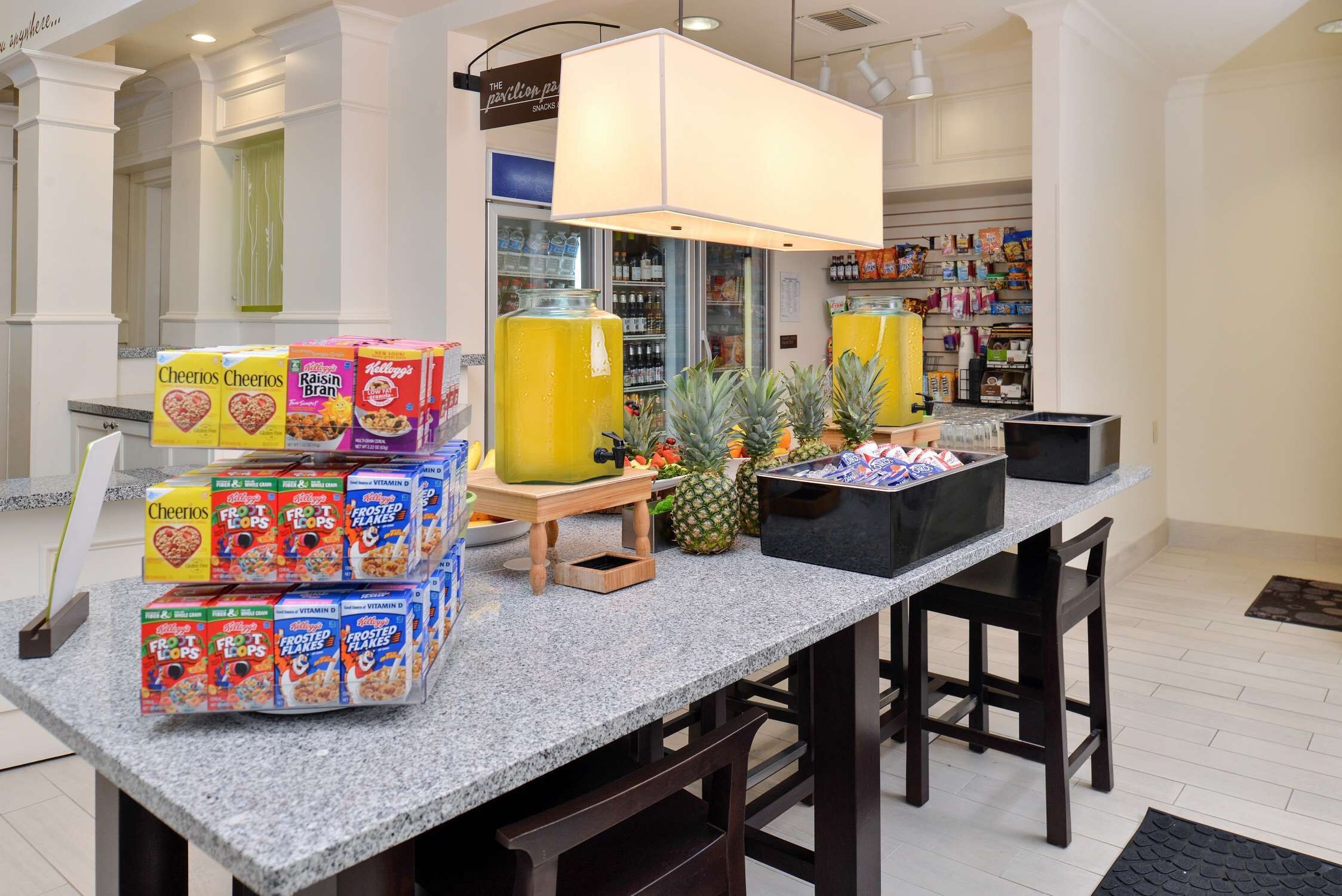 Un comptoir pour le petit-déjeuner avec des boîtes de céréales, une présentation de fruits et un réfrigérateur en arrière-plan.
