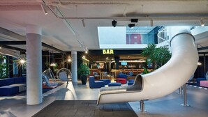 A modern indoor space with a slide, seating areas, and a bar. - HUP (Mierlo)