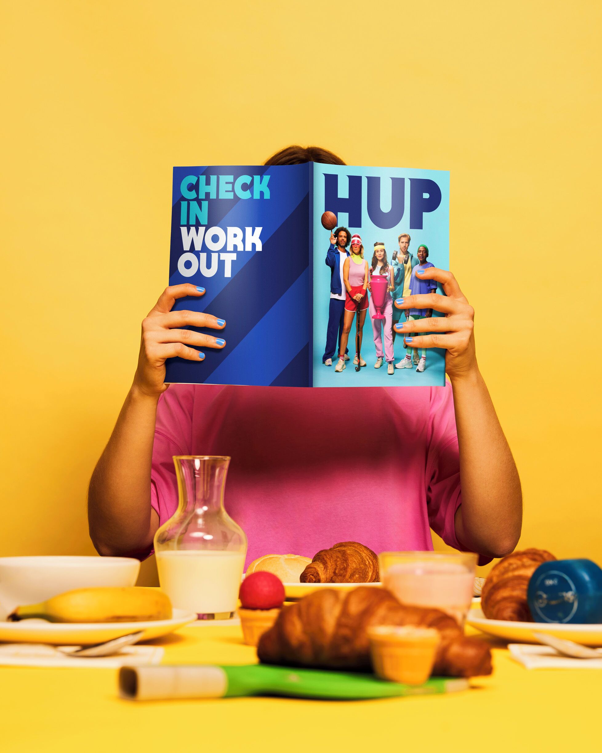 Een persoon houdt een boek vast, getiteld 'CHECK IN WORK OUT', met een groepsillustratie op de omslag.