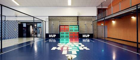 Una cancha deportiva interior con piso azul, un balón de fútbol y una pared con el texto 'HUP'.