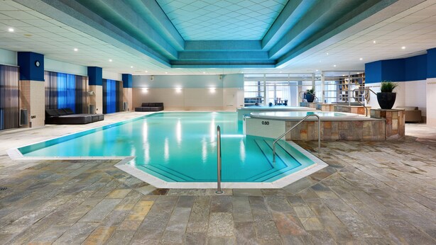 An indoor swimming pool with a tiled floor, a safety railing, and a clear view of the pool area. - HUP (Mierlo)