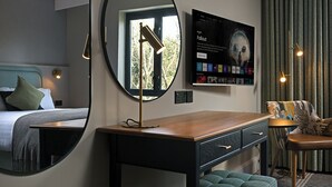 A hotel room with a bed, a desk, a chair, a round mirror, a TV, and a window with curtains. - Parkavon Hotel (Killarney)