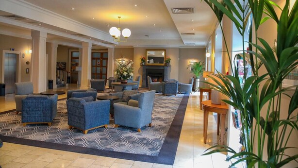 A spacious lobby with a modern design, featuring a seating area with sofas and armchairs, a large decorative plant, and a fireplace. - Parkavon Hotel (Killarney)