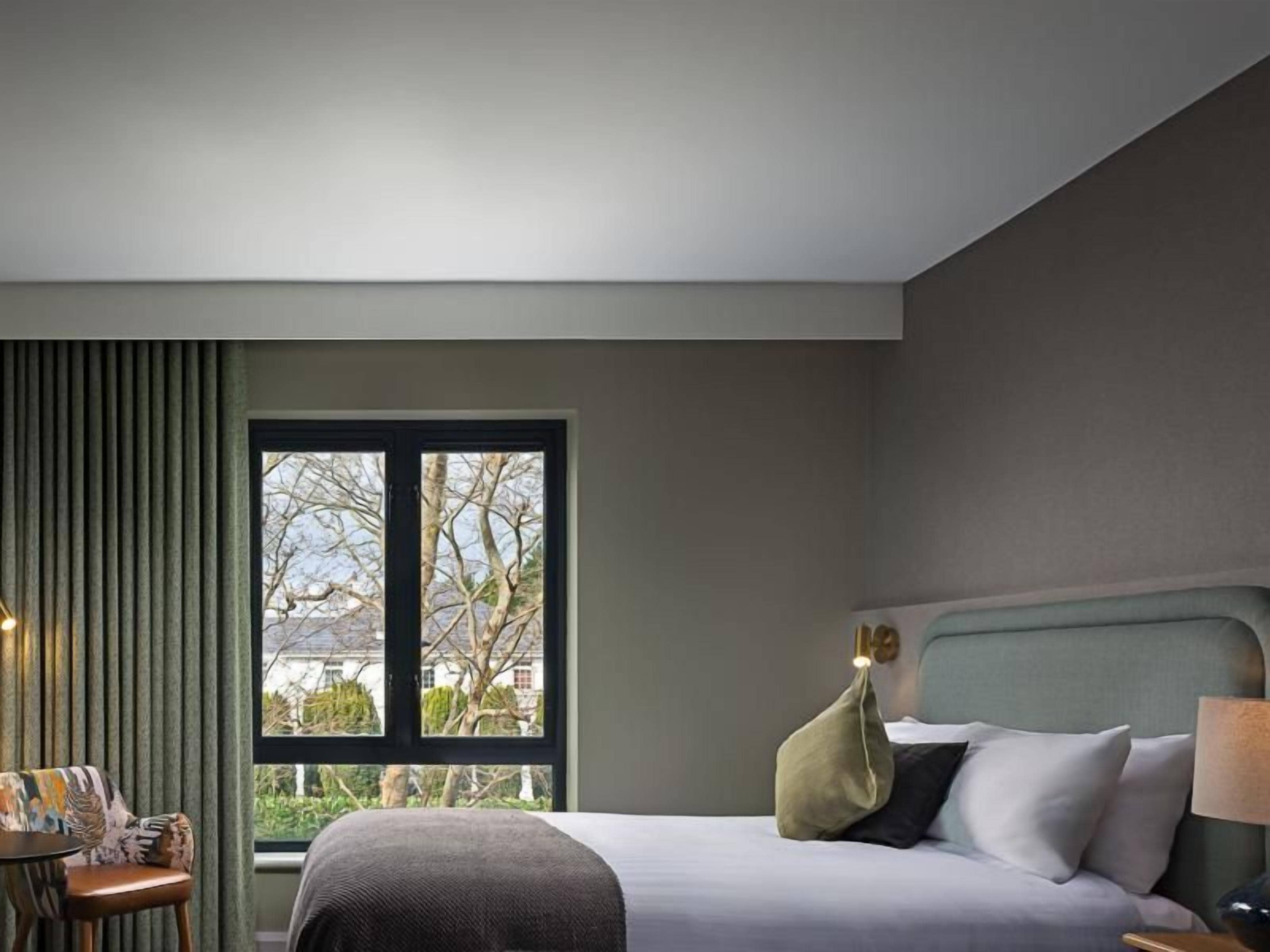 A hotel room with a bed, a window, a nightstand, and a chair.