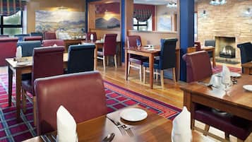 Un restaurante con varias mesas y sillas, piso de madera y una chimenea de piedra.