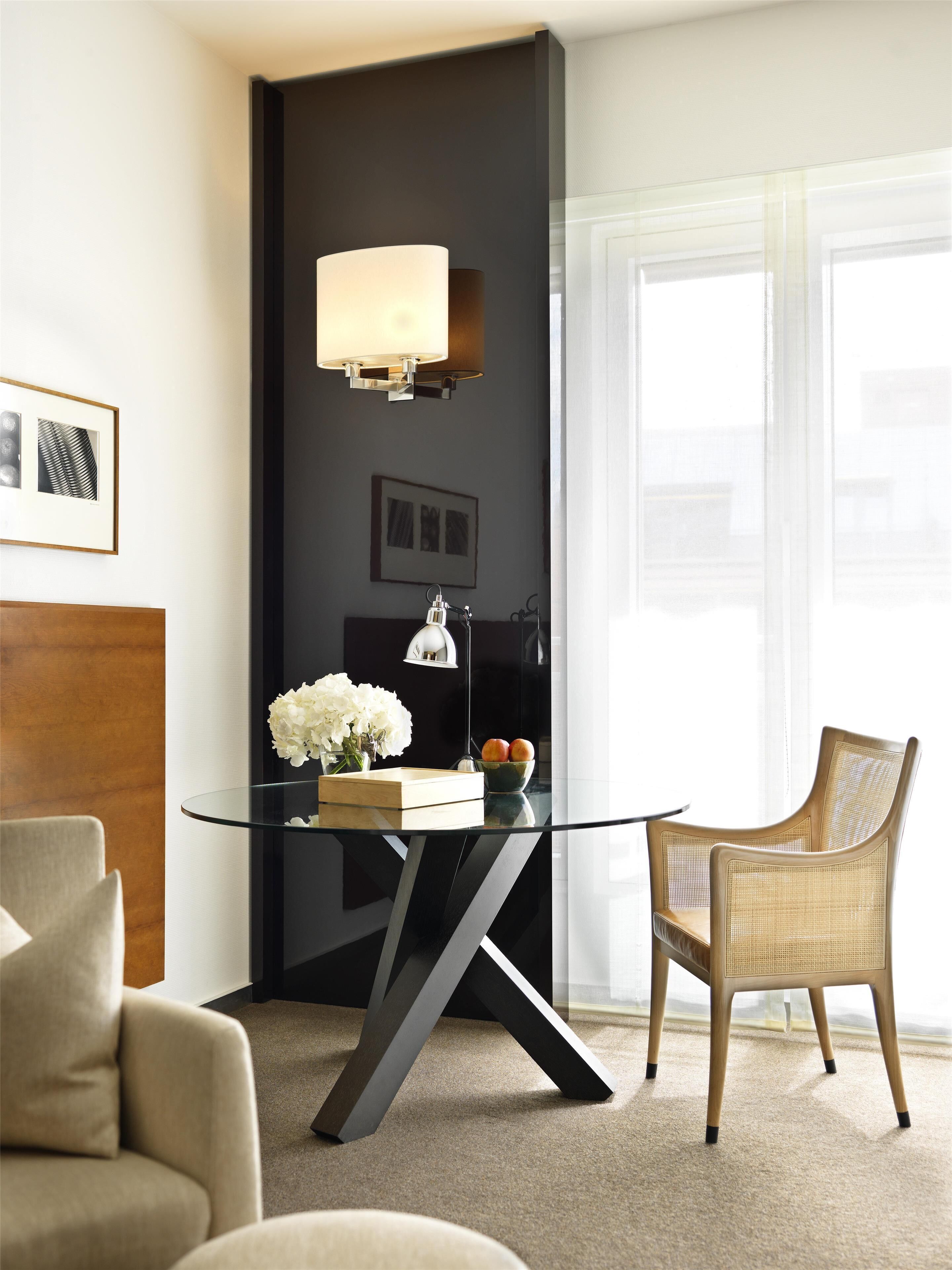 Una habitación moderna con una mesa de vidrio, una silla de mimbre, una lámpara y un jarrón con flores.