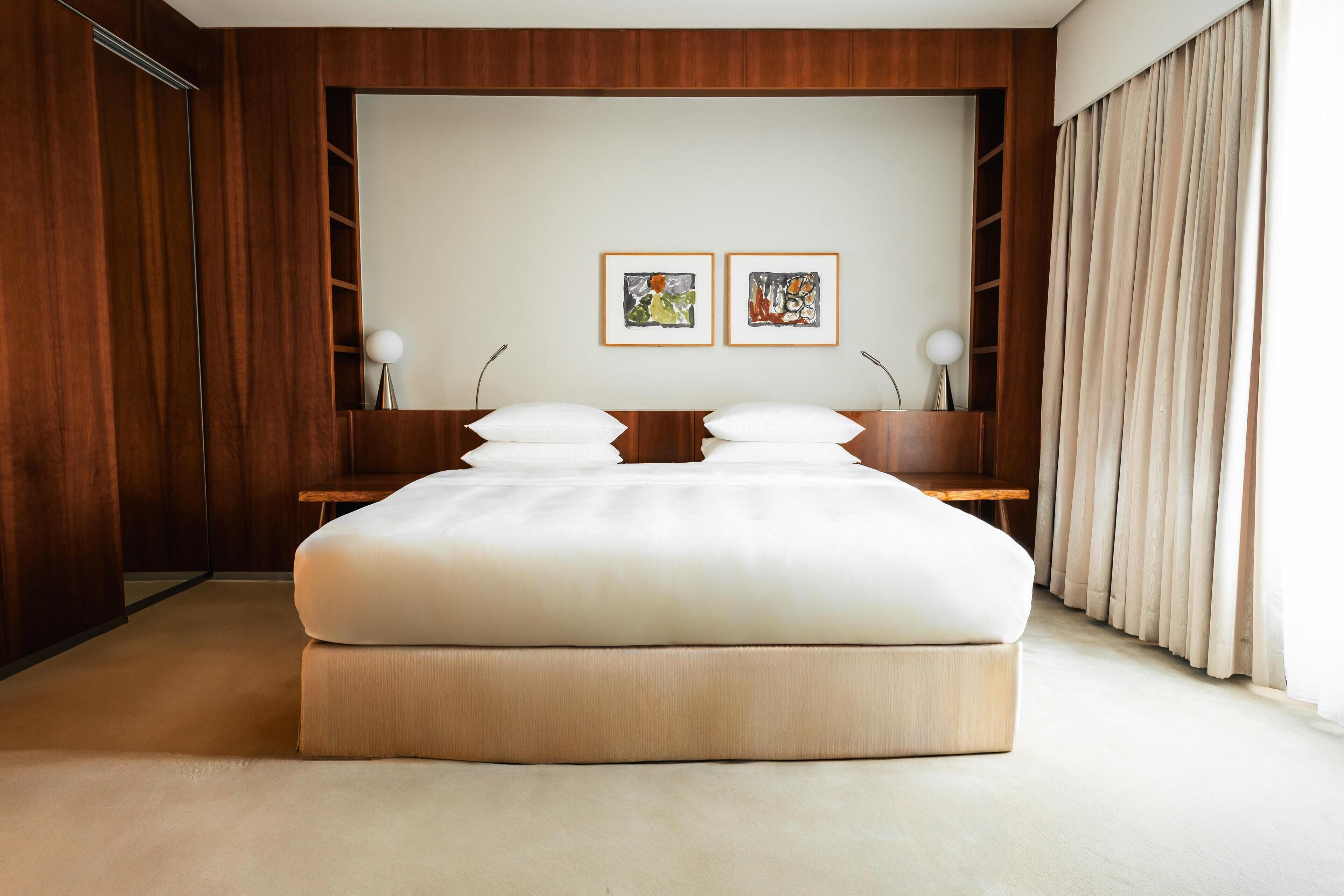 Un dormitorio moderno con una cama grande, paneles de madera, dos obras de arte enmarcadas y una mesita de noche con lámparas.