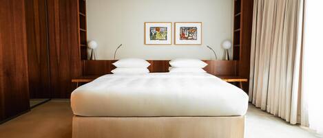 A modern bedroom with a large bed, wooden paneling, two framed artworks, and a bedside table with lamps.