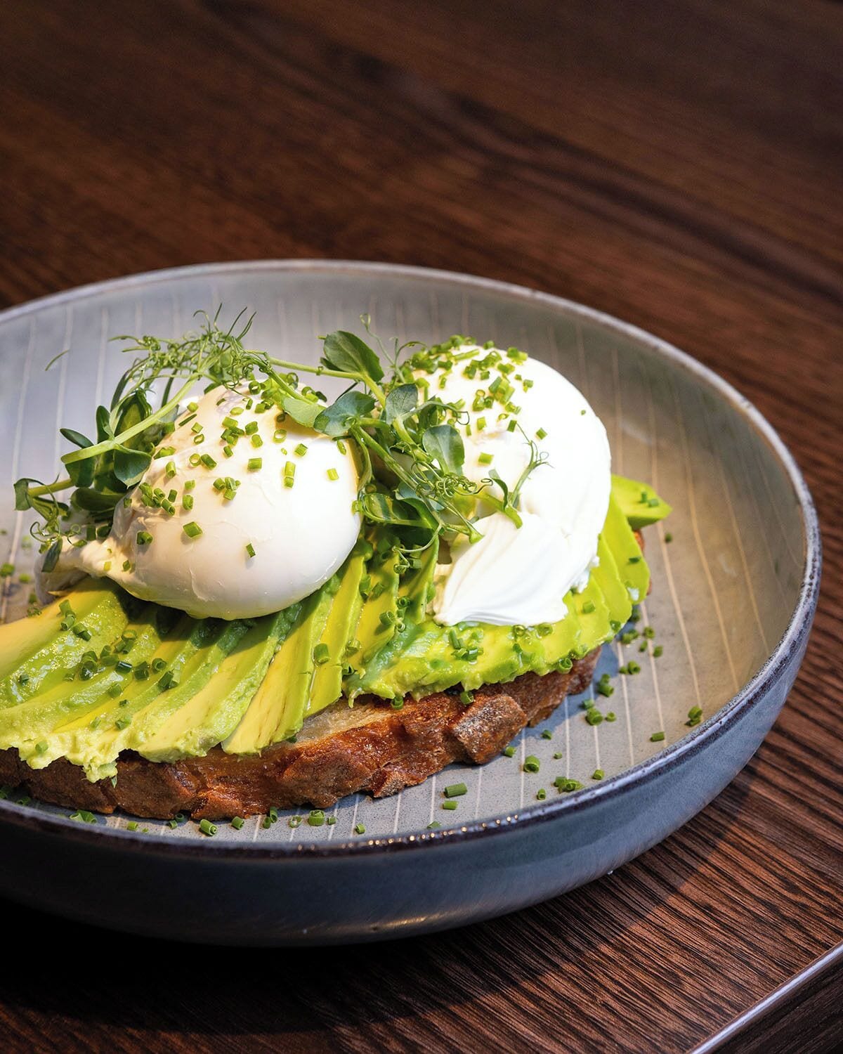 A plate with a poached egg, avocado slices, and green onions on toast.