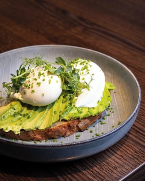 A plate with a poached egg, avocado slices, and green onions on toast. - Grand Hyatt Berlin (Berlin)