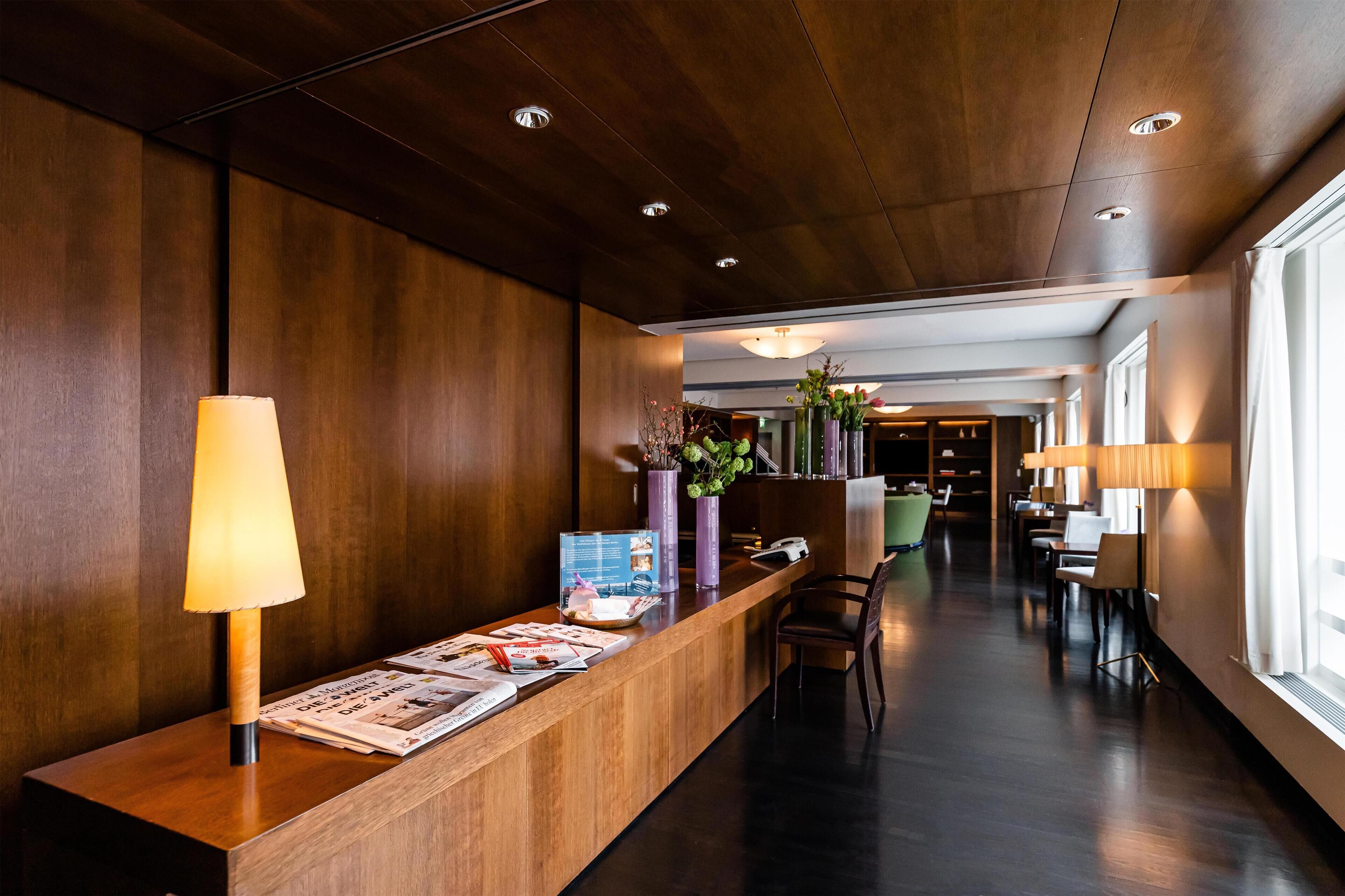 A reception area with a wooden reception desk, a lamp, magazines, and a vase with flowers.