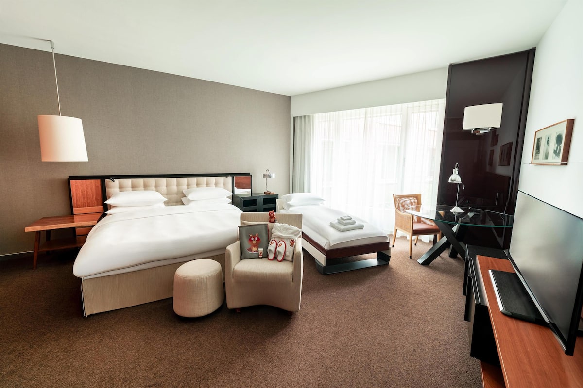 A modern hotel room with a large bed, a smaller bed, a desk, and a chair.