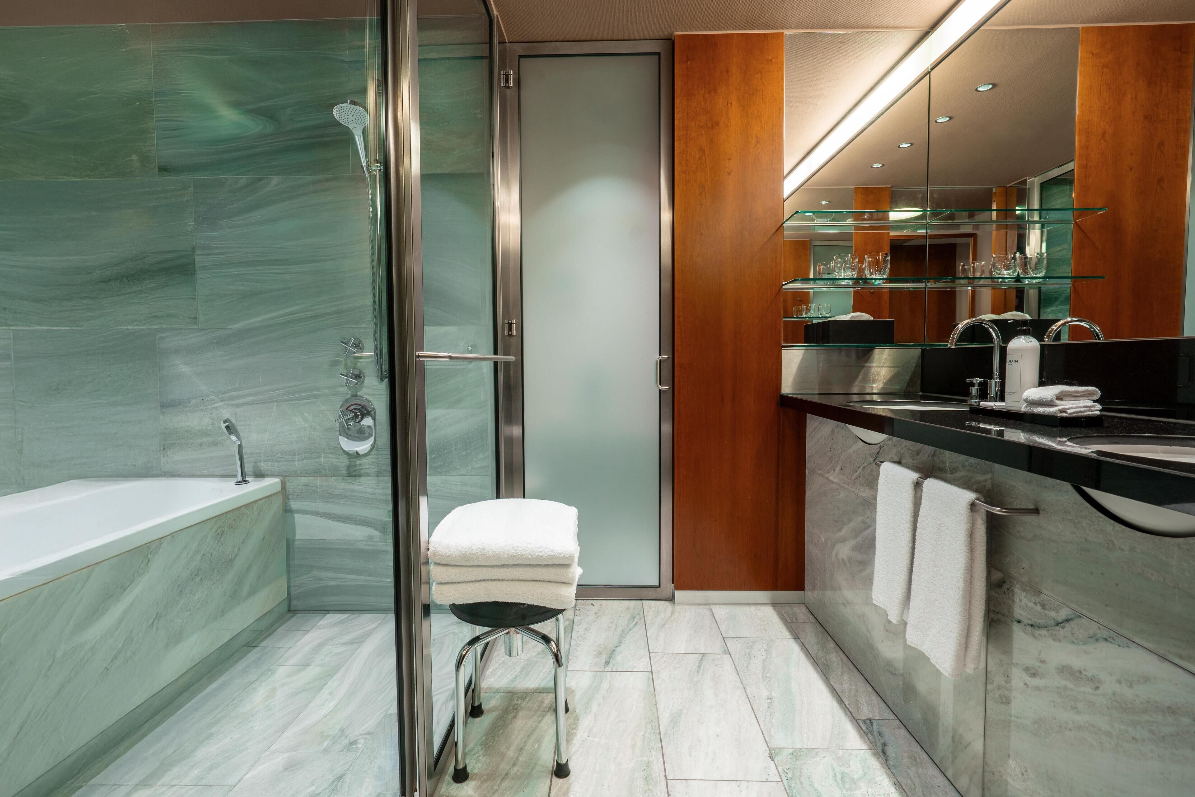 Un baño moderno con ducha acristalada, zona de lavamanos separada con tocador y estante de vidrio sobre el lavamanos.