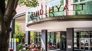 Grand Hyatt hotels facade med udendørs siddepladser og et stort træ i forgrunden.
