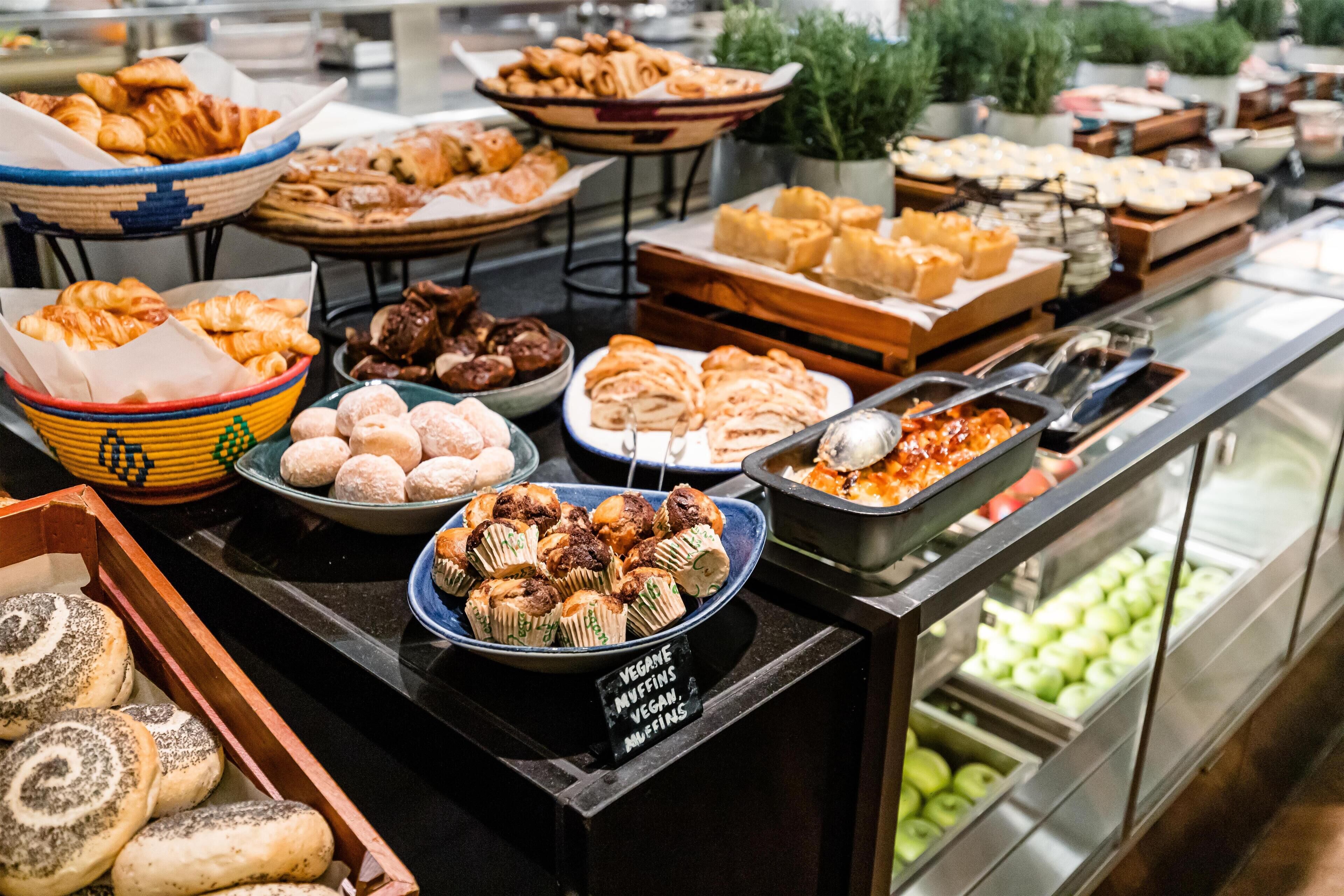 Un bufé con diversas opciones de comida, incluyendo muffins veganos, pasteles y otros postres.