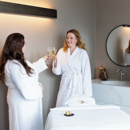A hotel room with a bed, a round mirror, a sink, and a vase with flowers.