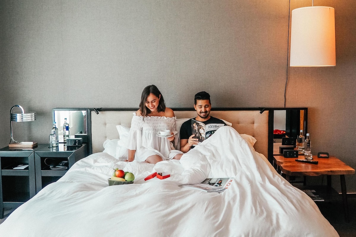 A hotel room with a bed, bedside tables, a lamp, and a mirror.