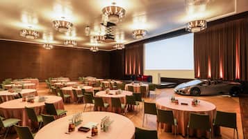 Un salón de conferencias con varias mesas redondas, sillas verdes y candelabros modernos.