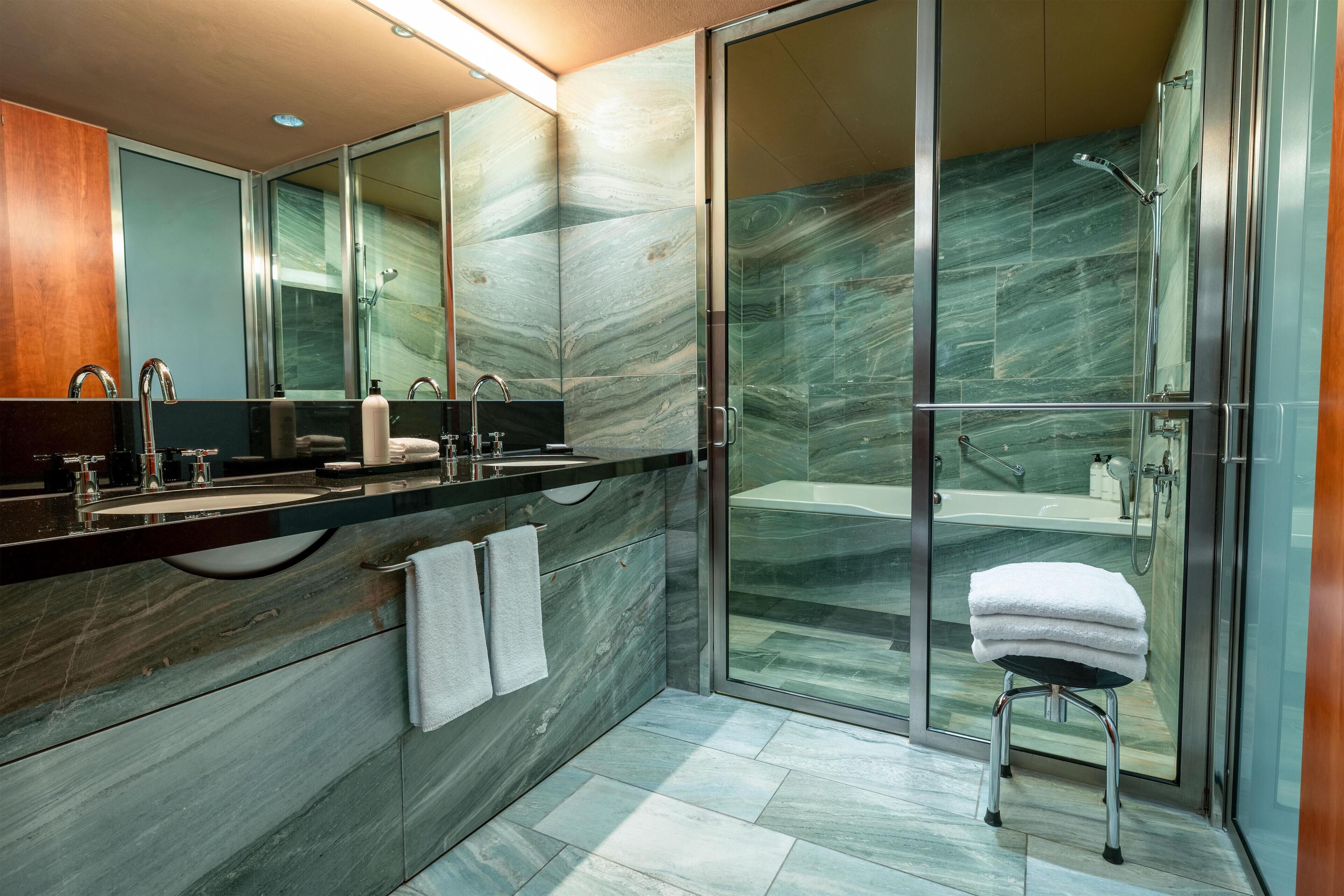 Un baño moderno con un espejo grande, dos lavamanos, una ducha y cabina de ducha con paredes de vidrio.