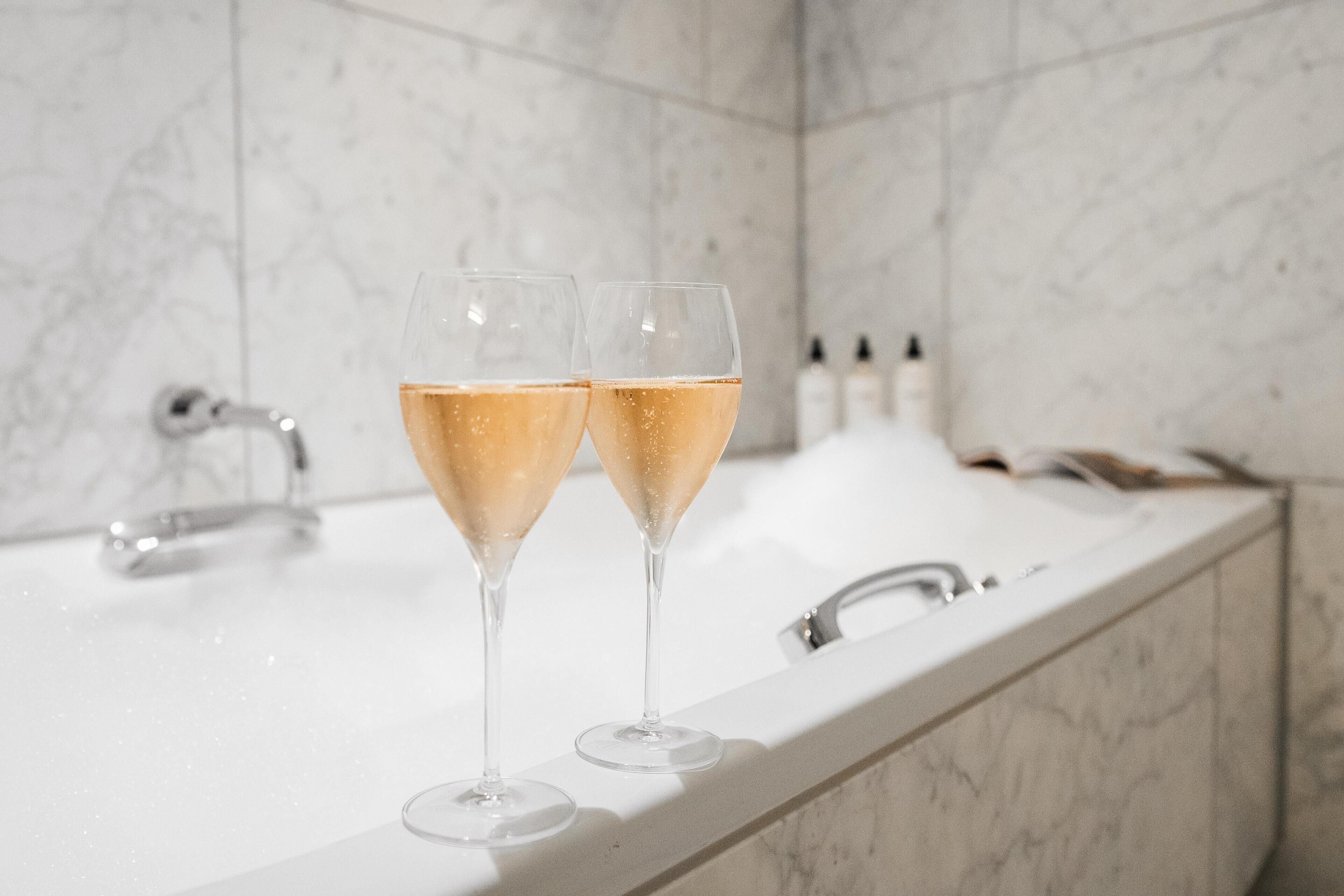 Två champagneglas på en bänkskiva av marmor i ett badrum med modern design.