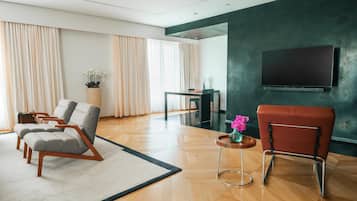 Una sala de estar moderna con un televisor de pantalla plana, dos sillones grises, un sillón rojo, una mesa de centro de madera y una planta en maceta.