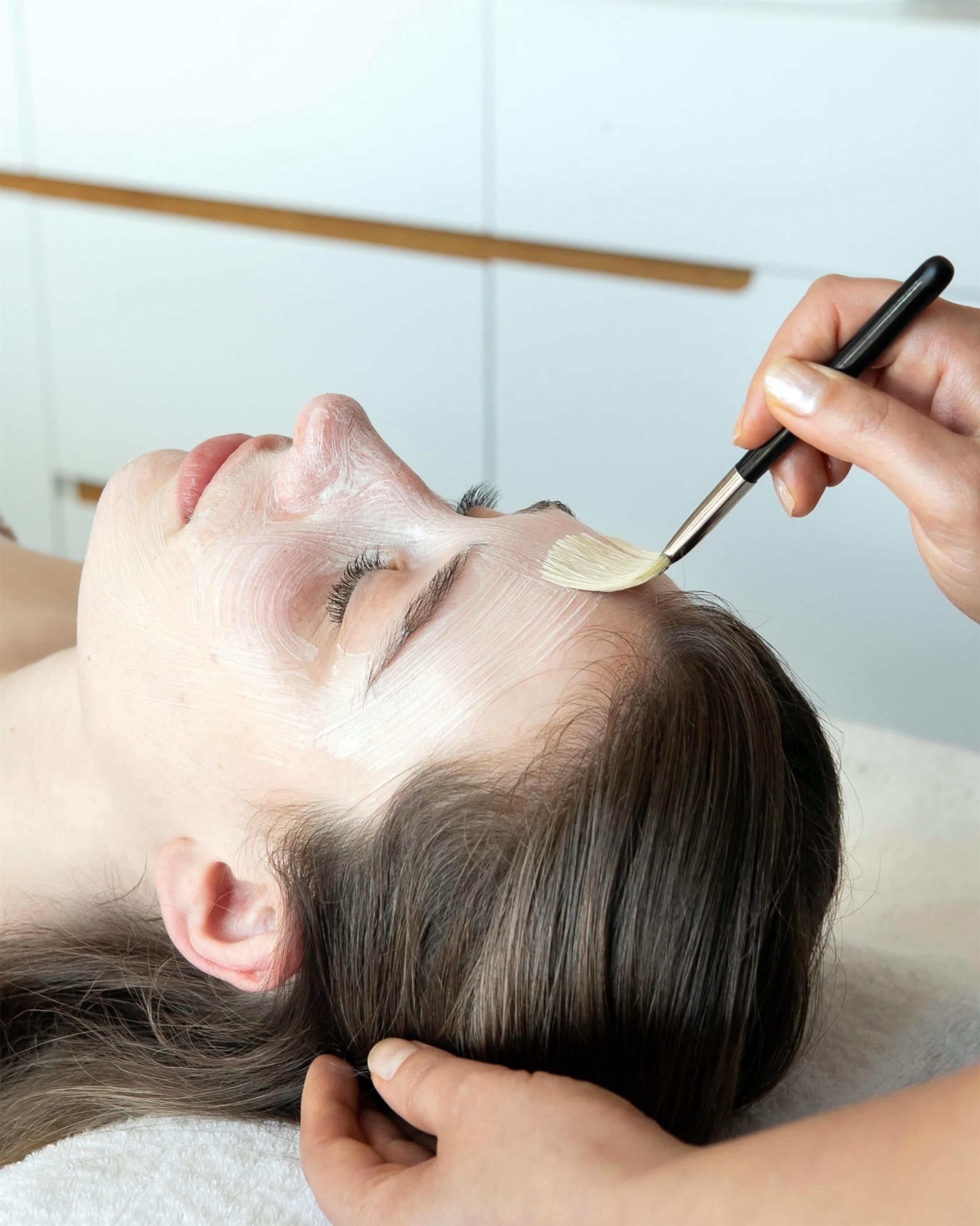 A person lying down with a hand applying a substance to their forehead.