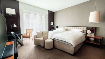 A modern hotel room with a large bed, a desk, a chair, and a TV.