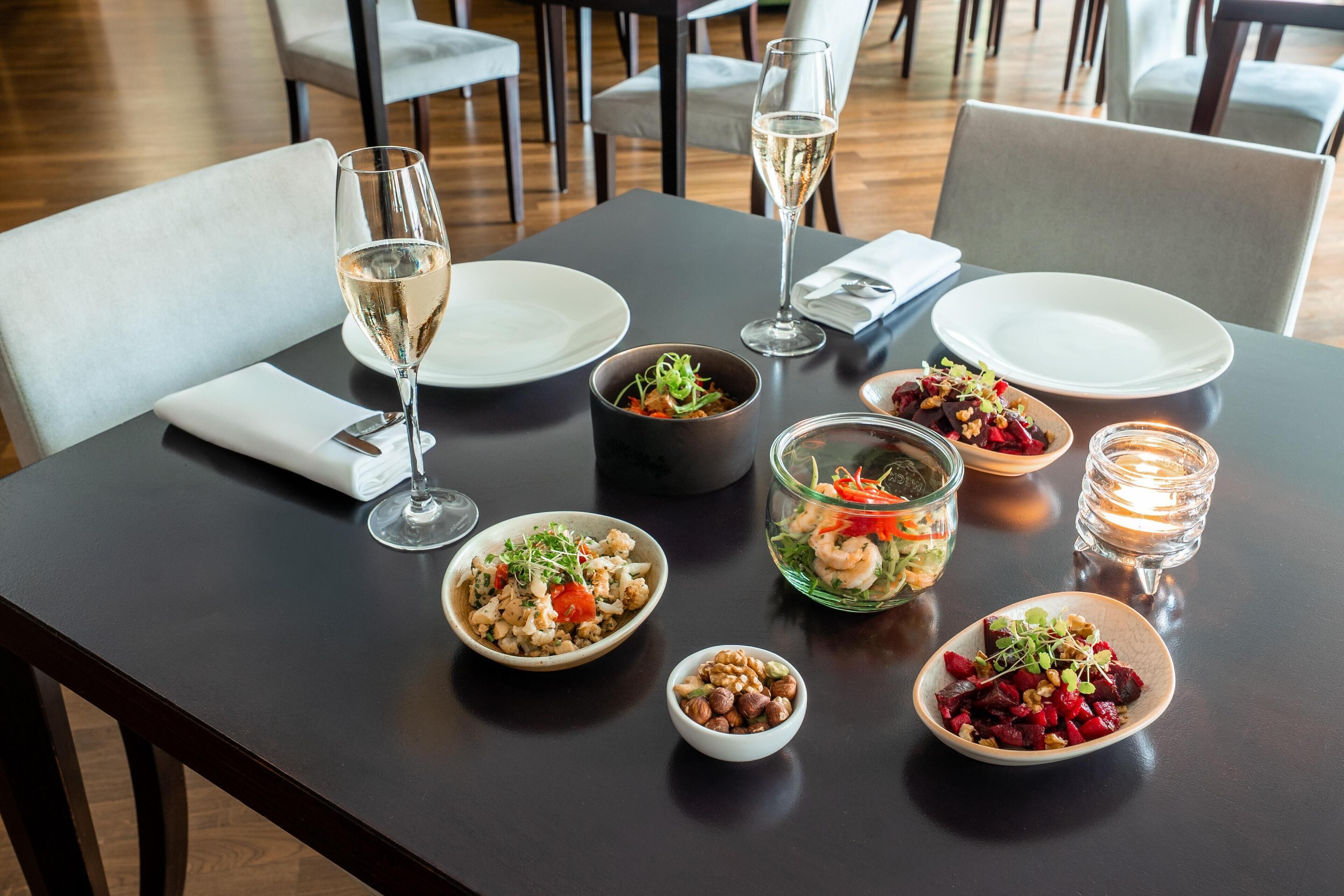 A dining table set with plates, bowls of food, glasses of wine, and candles.