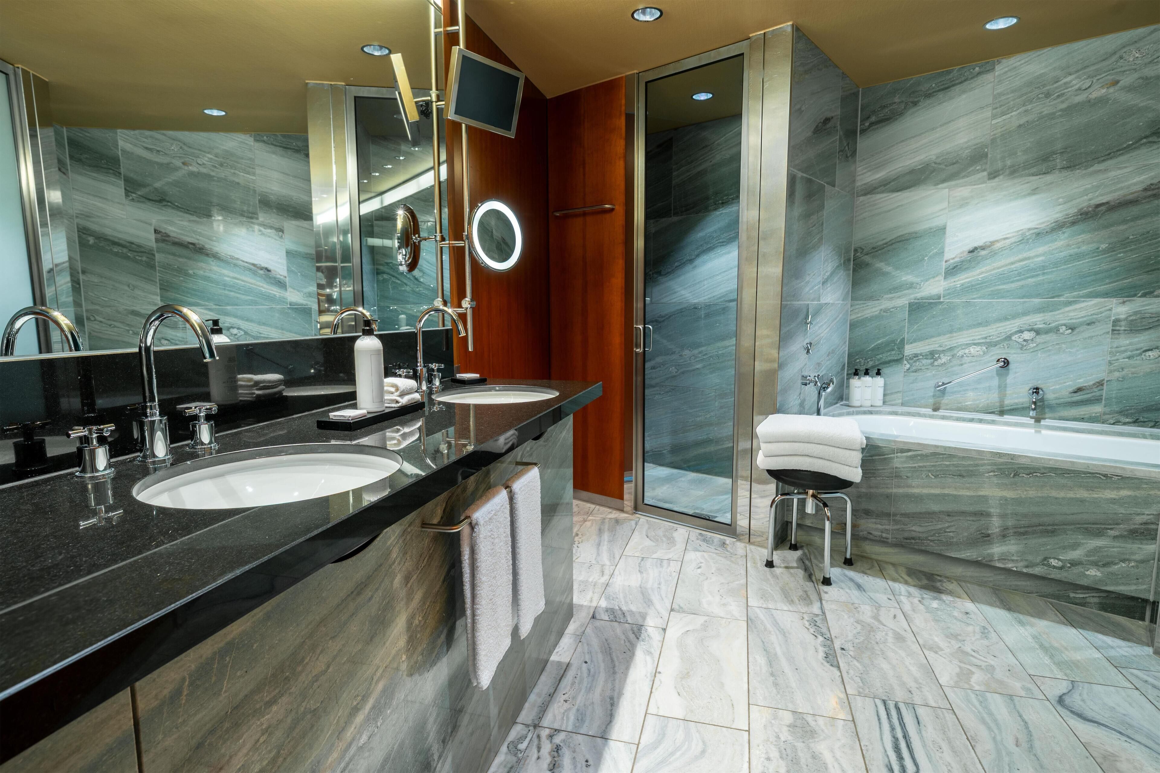 A modern bathroom with two sinks, a large mirror, a vanity, and a bathtub.