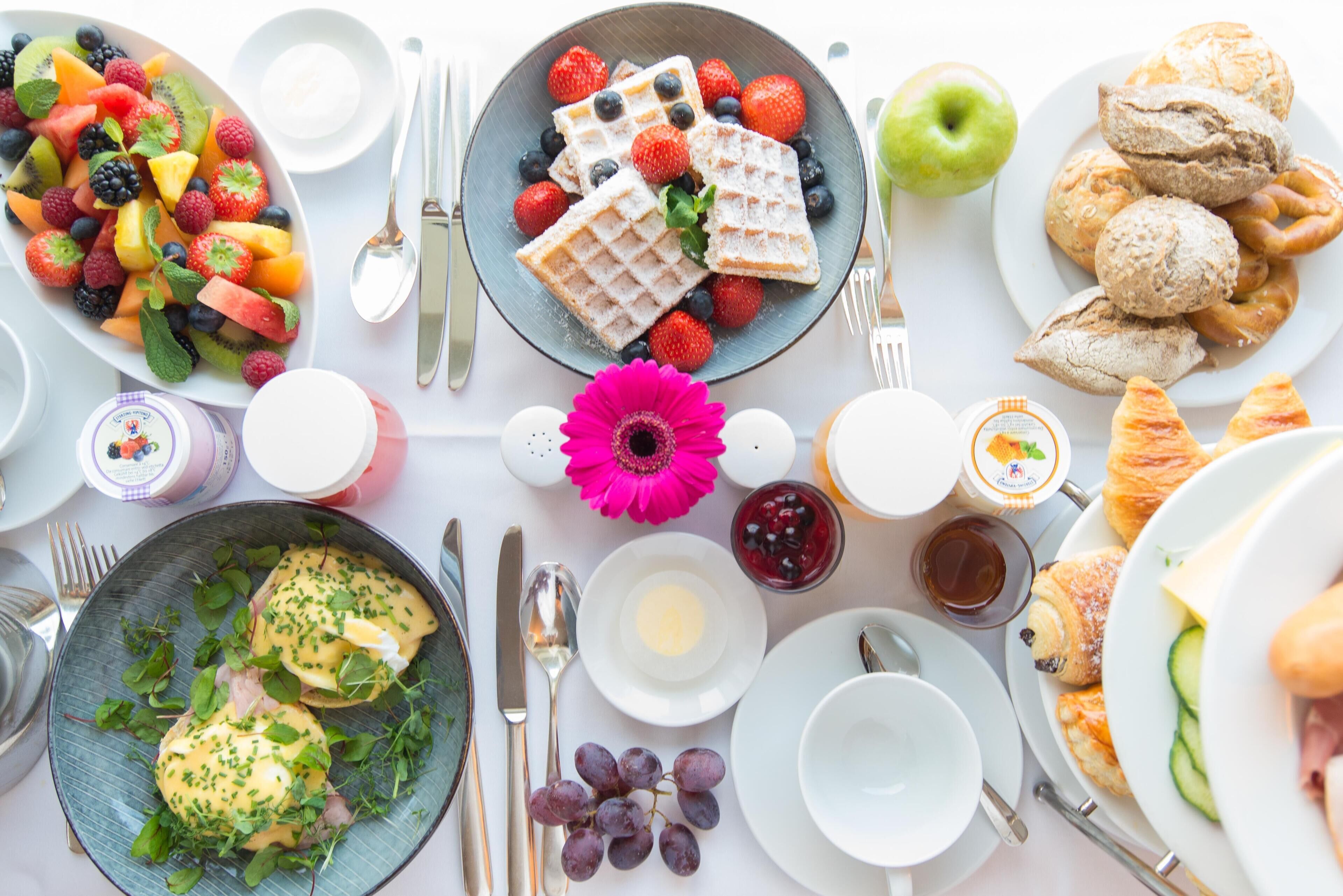 Un desayuno con una variedad de platillos, incluyendo waffles, fruta, pasteles y huevos Benedict.